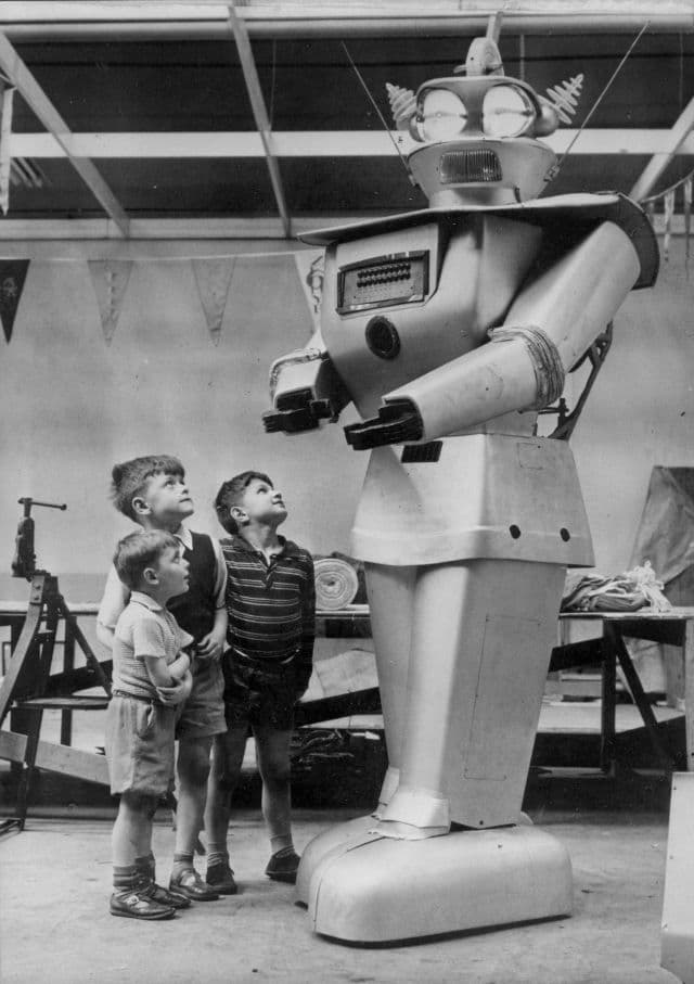 The image is black and white and shows three children looking up at a large robot. 